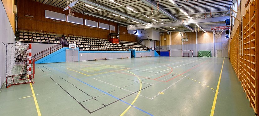 En tom sporthall med handbollsmål och läktare. 