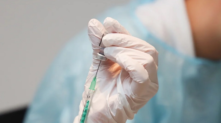 Platshandskebeklädd hand drar ut vaccin ur en ampull.
