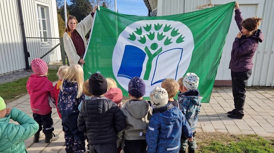 Barn och pedagoder som står och håller upp en grön flagga. Karungi förskola har certifierats med Grön flagg. Foto : privat 