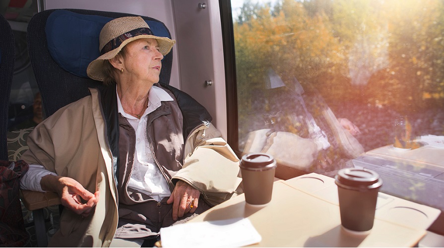 Äldre kvinna sitter vid ett tågfönster och tittar ut