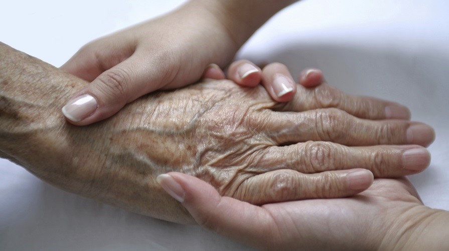 En yngre kvinnas hand håller en äldre kvinnas hand.