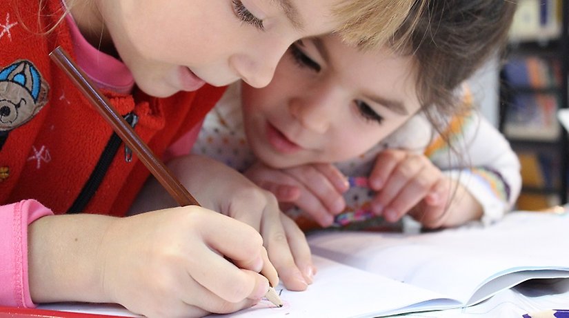 Två små flickor skriver och ritar i en bok med en färgpenna.