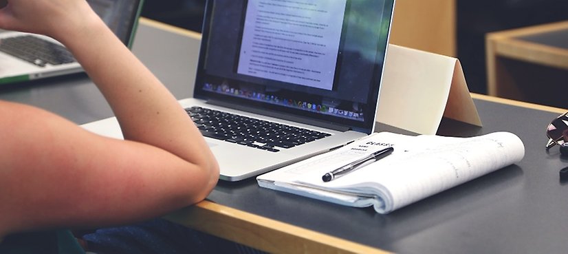 En bärbar dator, block och penna på ett arbetsbord.