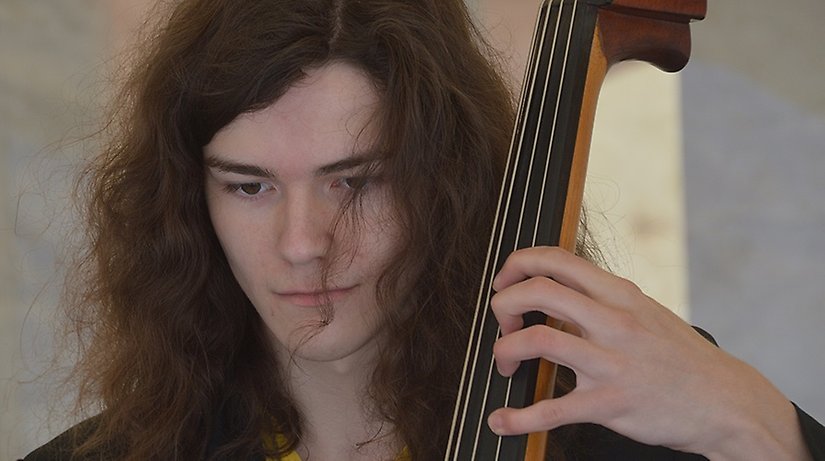 Ung man med långt hår spelandes på en cello.