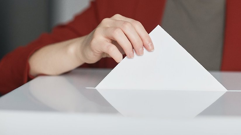 Svartvit bild på en hand som lägger ett kuvert i låda.