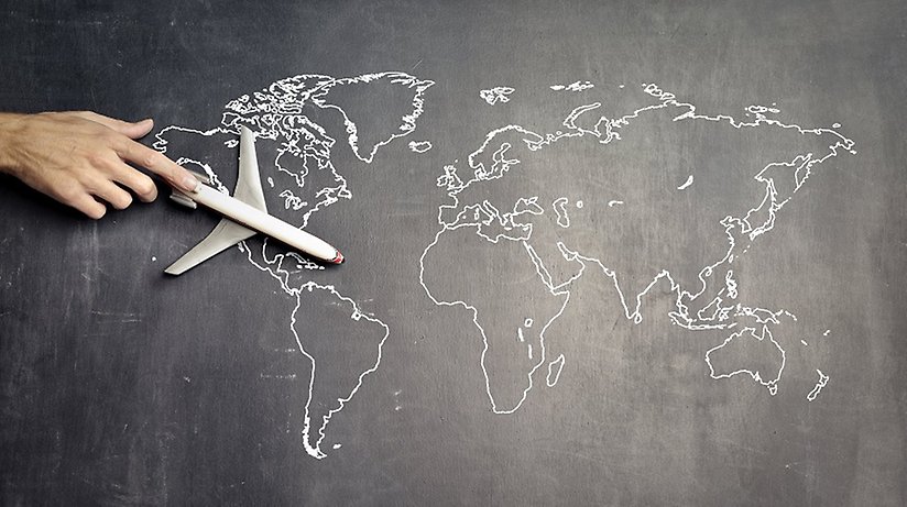 Världskarta rotat på en svart tavla. En hand håller i ett leksaksflygplan framför kartan.