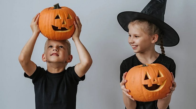 Två barn klädda i svart håller i varsin pumpa. Pumporna är gjorda för halloween.