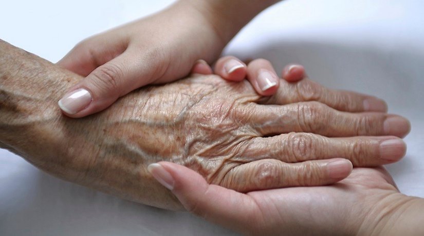 Närbild på en yngre persons hand som håller en äldre persons hand.
