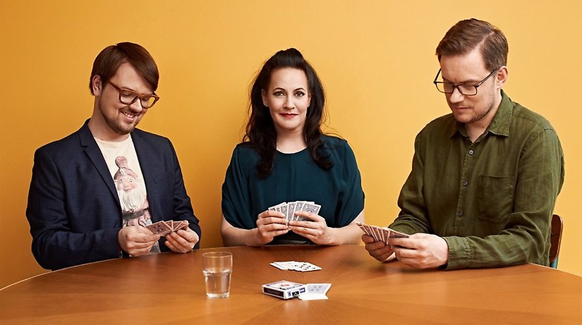 Två män och en kvinna sitter vid ett bord och spelar kort.
