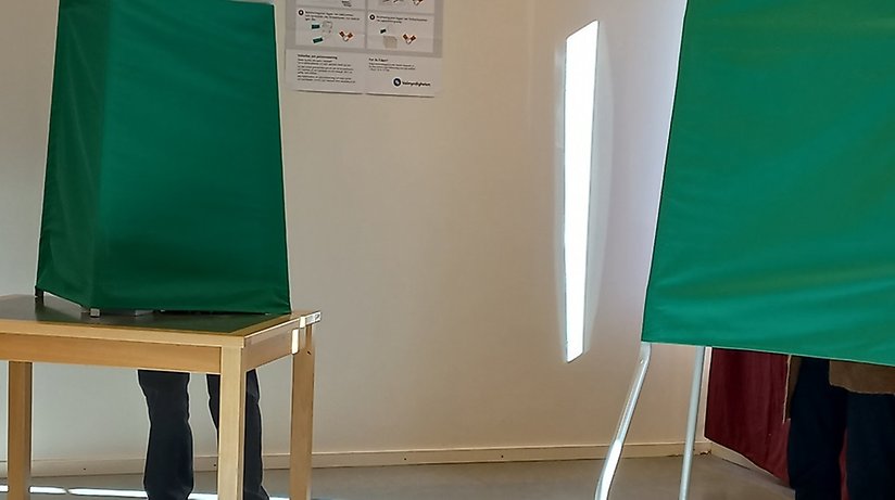 Två gröna röstningsbås i vallokalen på Haparanda stadsbibliotek. Nedtill, bakom båsen syns ben på personer som är och förtidsröstar. Foto: Haparanda stad 