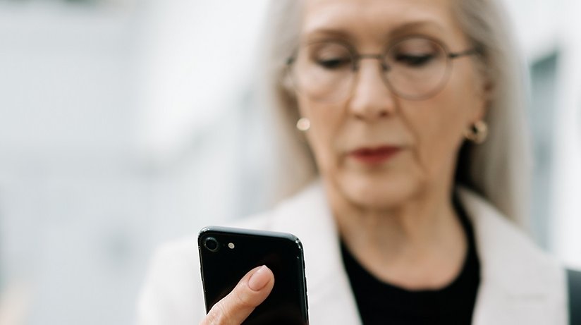 Äldre kvinna klädd i vitt tittar på en smartphone.
