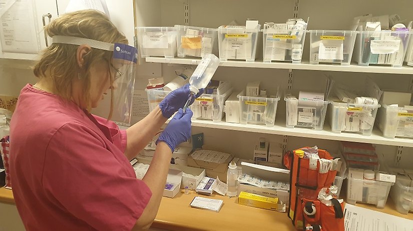 En kvinnlig sjuksköterska står i ett laboratorium och möter upp saltlösning. 